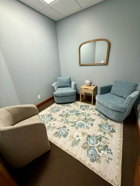 The waiting room at Anchor Within Counseling in Hamburg, NY with two plush blue armchairs, a small side table, a mirror, and a floral rug — a quiet, welcoming spot to settle in before your session.